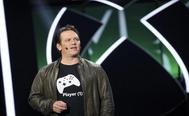 Phil spencer wearing xbox console controller black t shirt speaking on stage with xbox logo in background